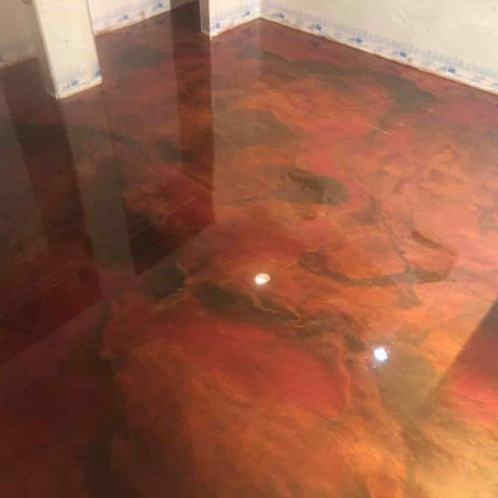 Metallic epoxy floor with red, orange, and gold swirls, reflecting light in a room.