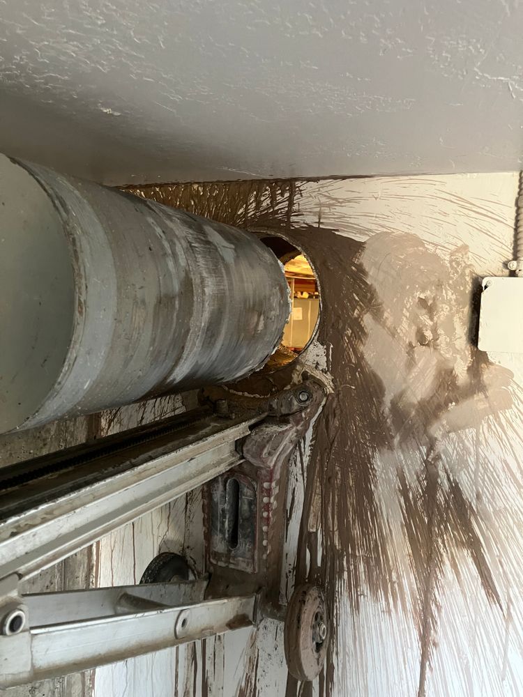 A large, industrial drill boring through a wall, covered in wet, muddy debris.