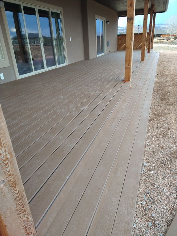 Brown composite deck with wood posts extending from a light brown exterior wall.