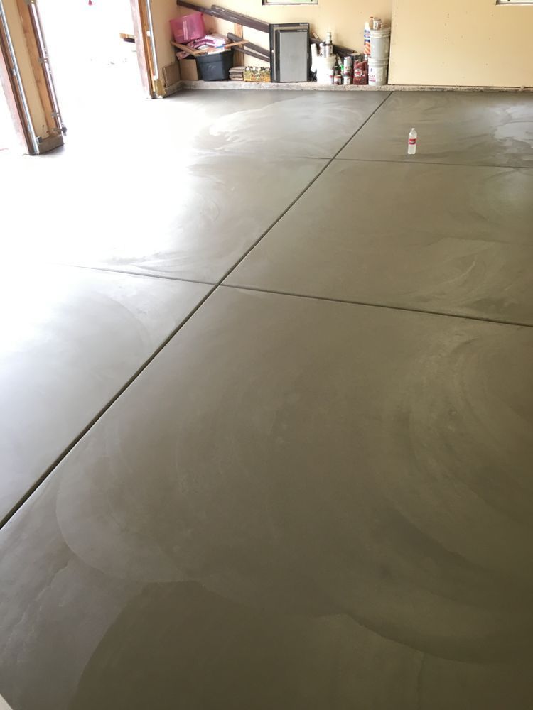 Newly poured concrete garage floor, with cut lines, light gray, with open garage door.