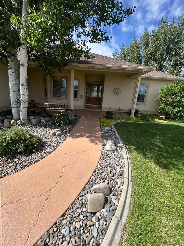 Tan house with a curved orange path leading to the front door, bordered by rocks and grass.