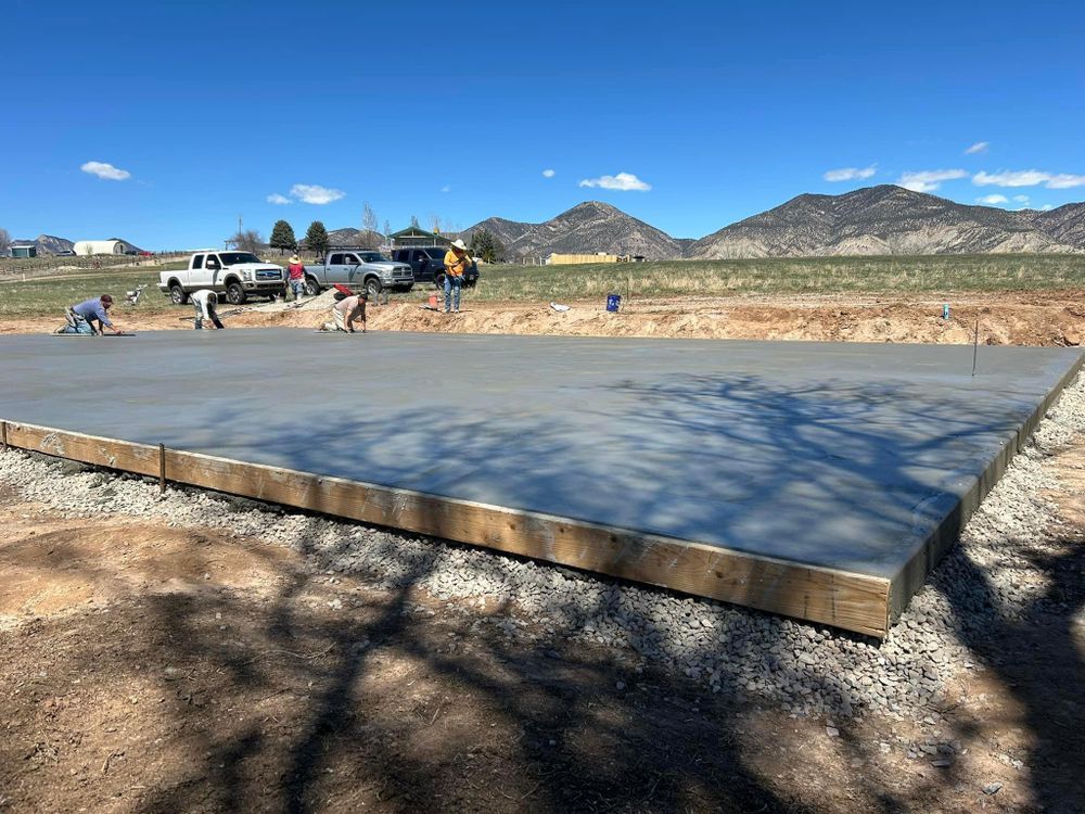 Workers smoothing fresh concrete slab on a construction site with mountains in the background.