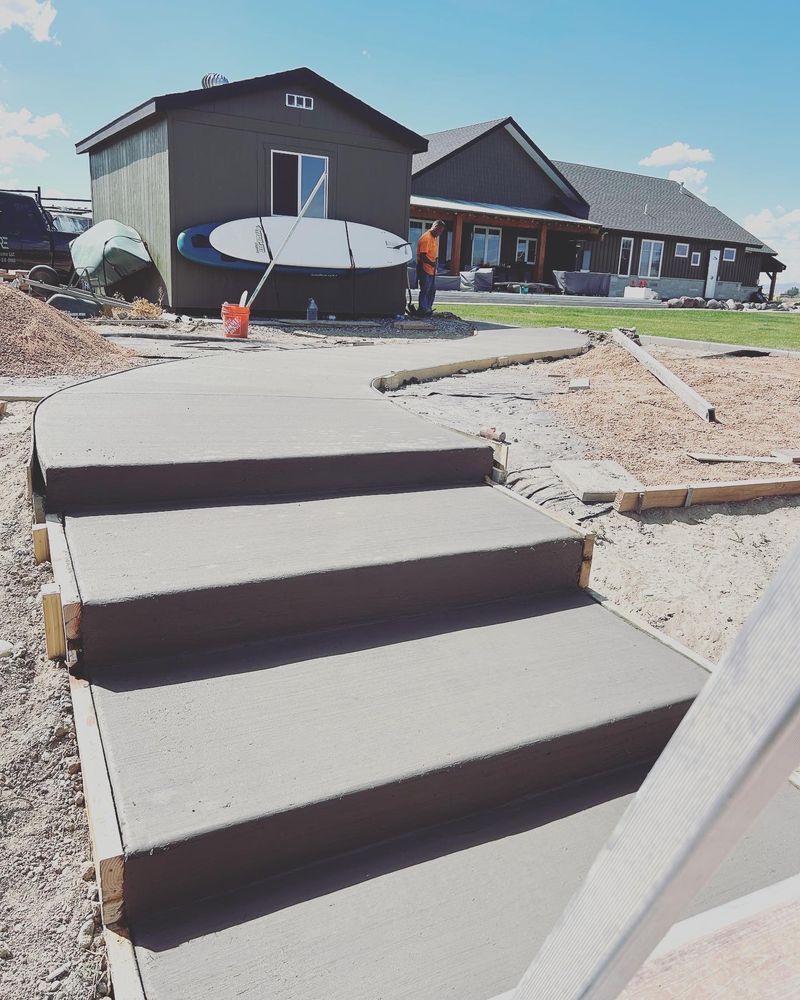 Concrete steps lead to a house under construction; a paddleboard leans against a shed.