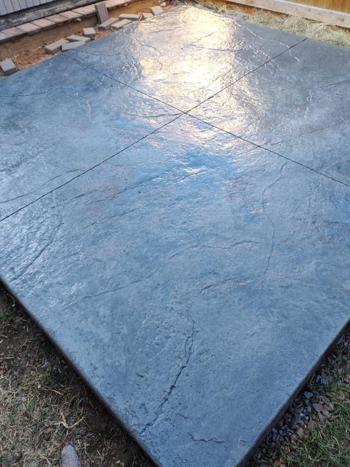 Finished, square, blue-gray stamped concrete patio with decorative lines and cracks, outdoor setting.