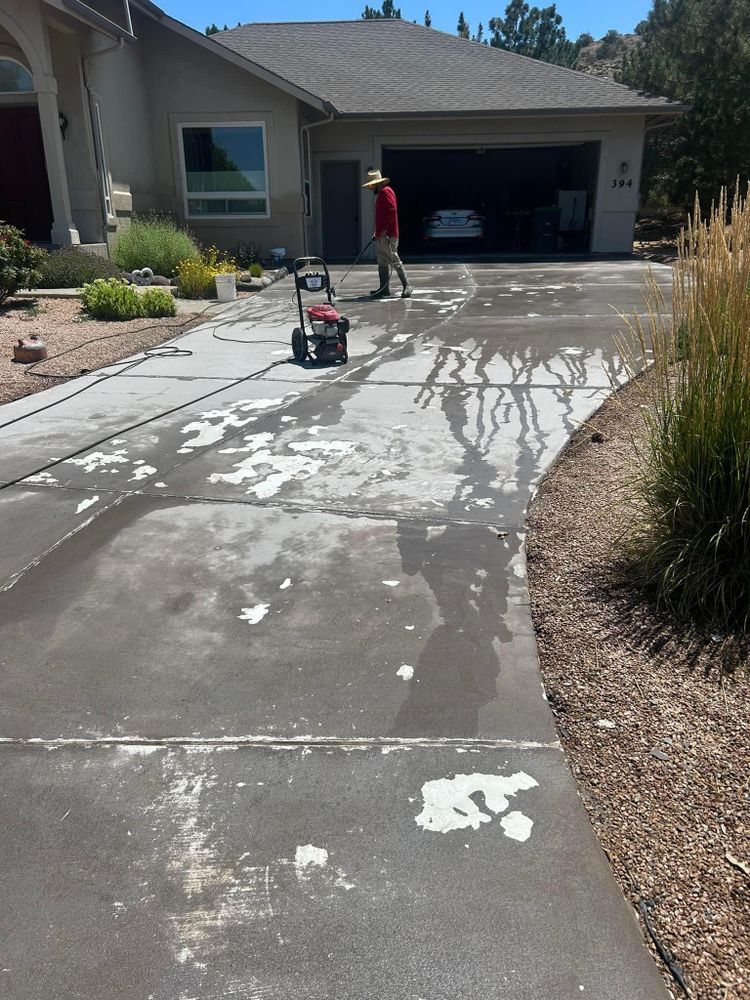 Person pressure washing a driveway in front of a house.