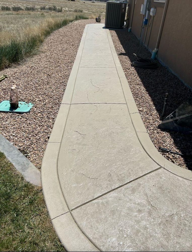 Concrete sidewalk curving past a house and rock landscaping.