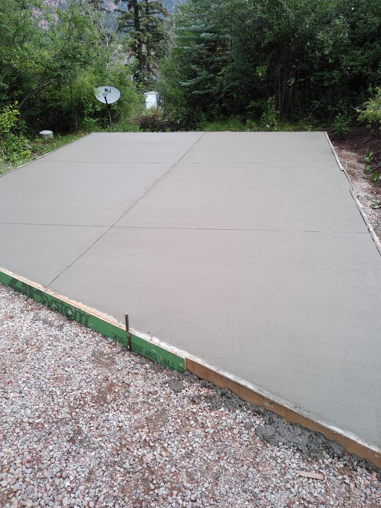 Newly poured concrete patio, bordered by wood and gravel, set in a yard.