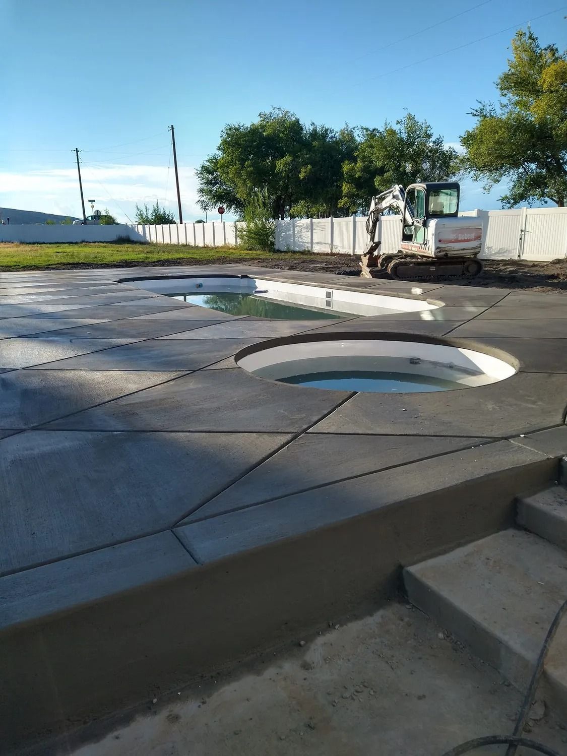 Concrete pool deck under construction with circular openings for pools, excavator in the background.