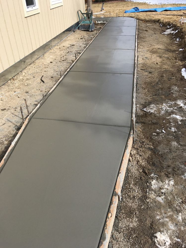 Freshly poured gray concrete walkway next to a building, framed by wooden borders.