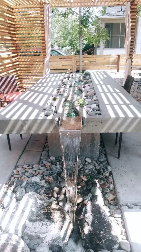 Concrete table with water feature, wood pergola, and surrounding stone patio.