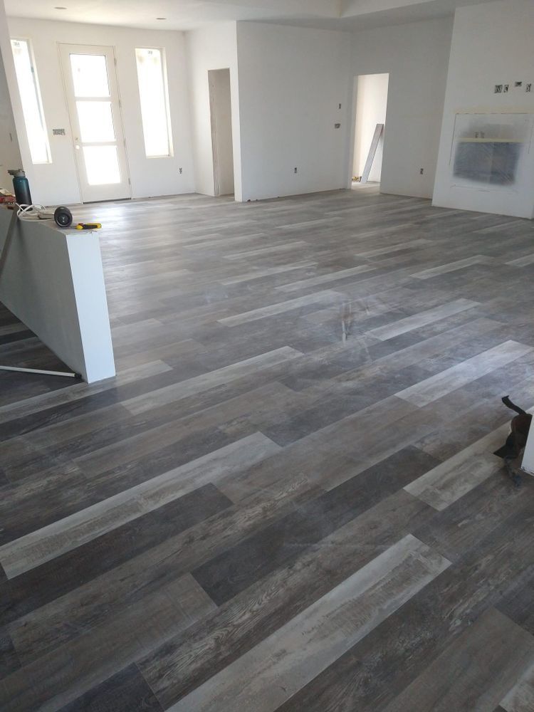 Gray wood-look floor tiling in a large, mostly empty room with white walls and natural light.