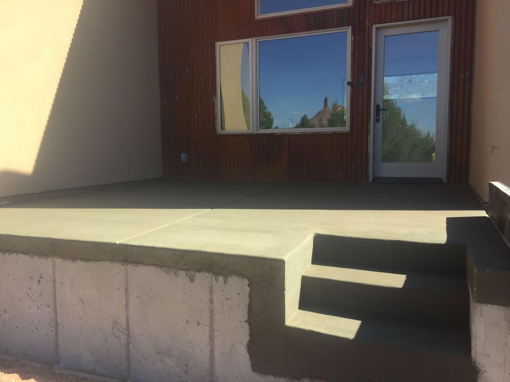 Concrete patio with two steps, door, and windows against a wood-paneled wall.