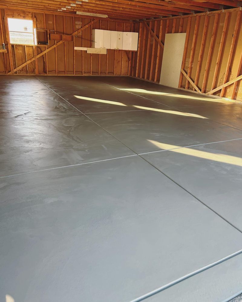 Newly poured concrete floor in a garage with wooden framing, sunlight casting shadows.