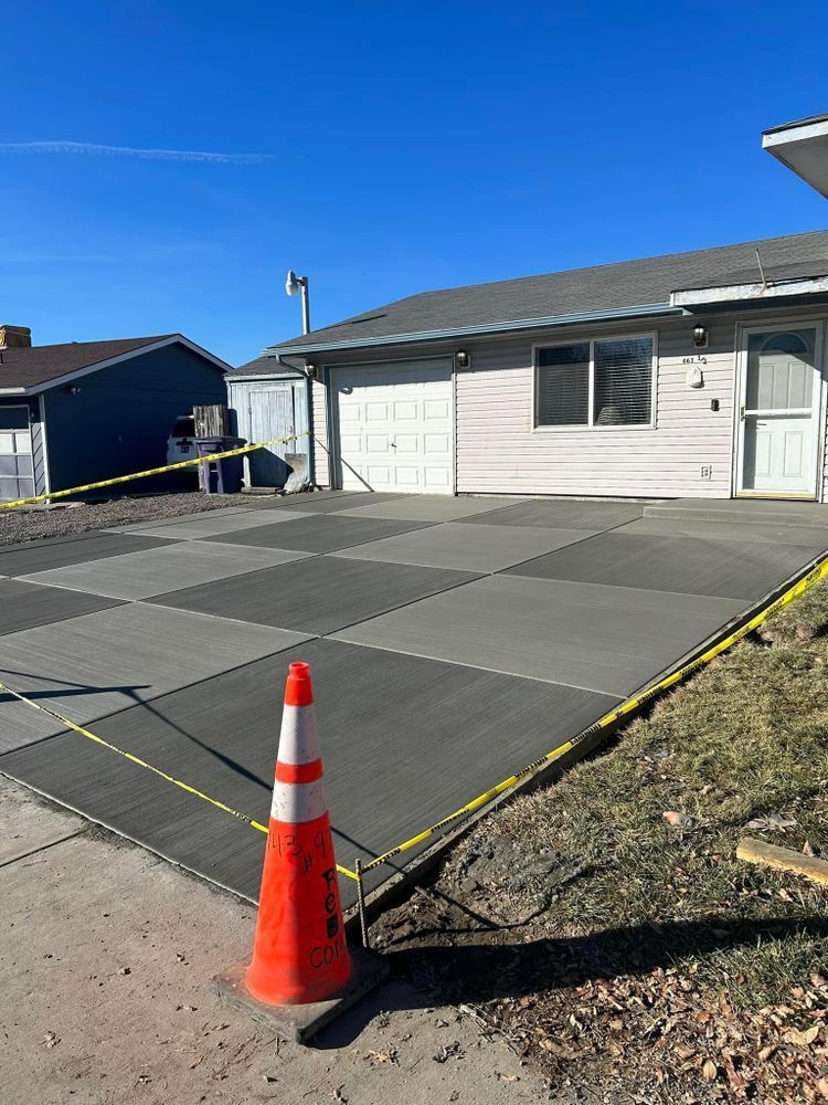 Newly poured concrete driveway with alternating gray and dark gray squares, caution tape, and a traffic cone.