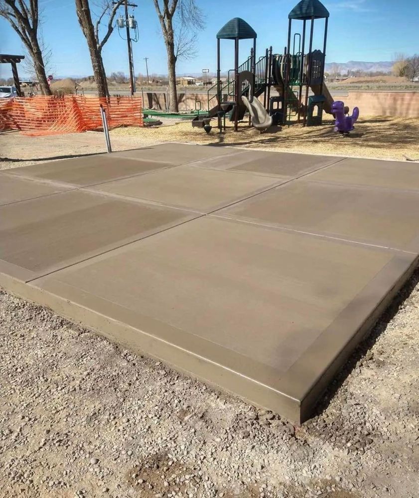 Newly poured concrete pad at a playground, with playground equipment in the background.