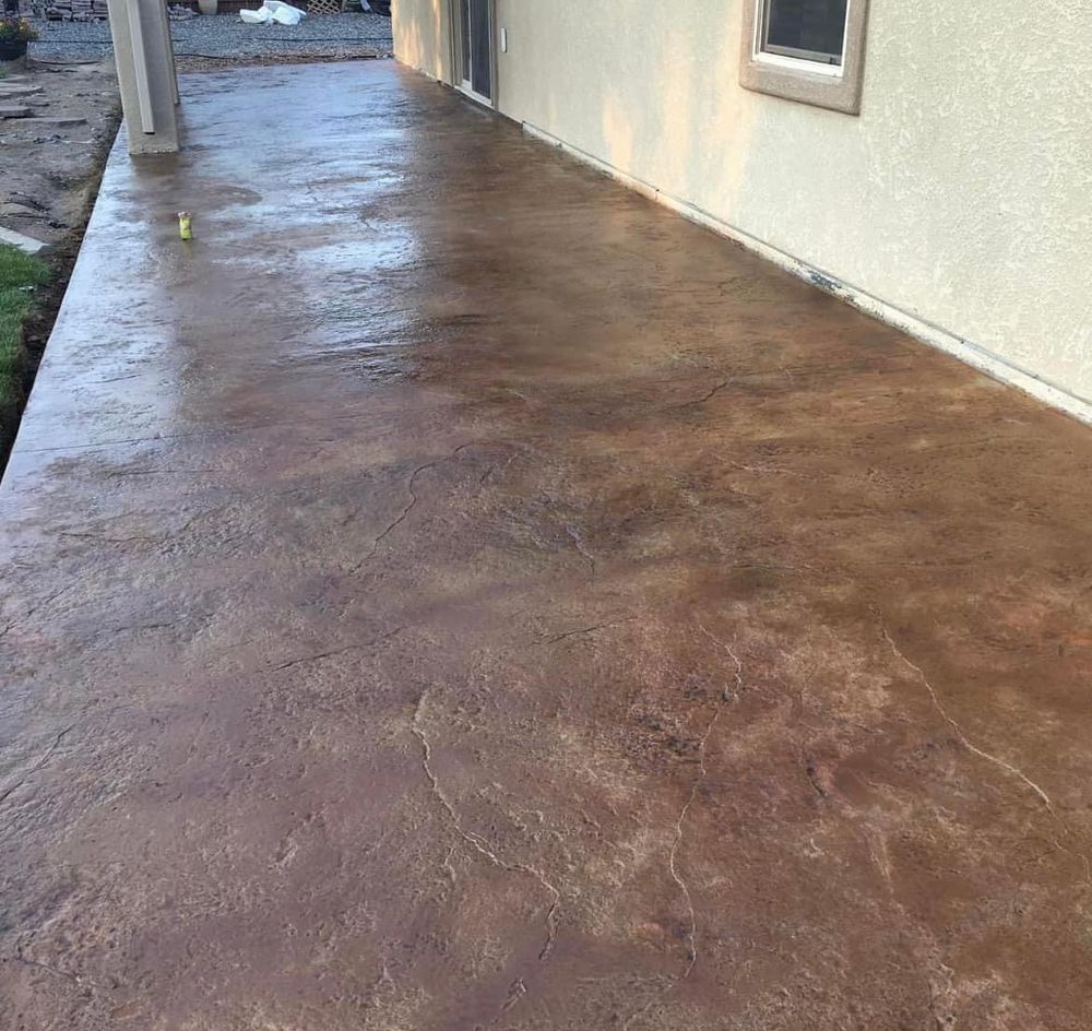 Brown, stained concrete patio next to a house with a window.