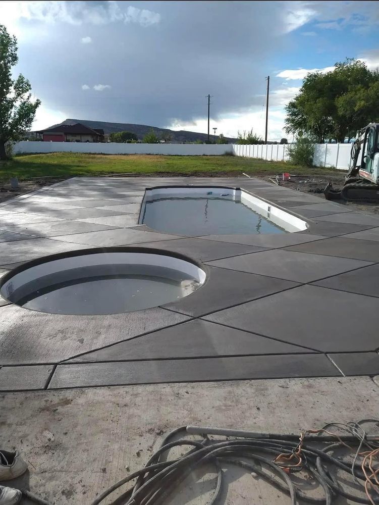 New concrete pool deck with two water features; cloudy sky.