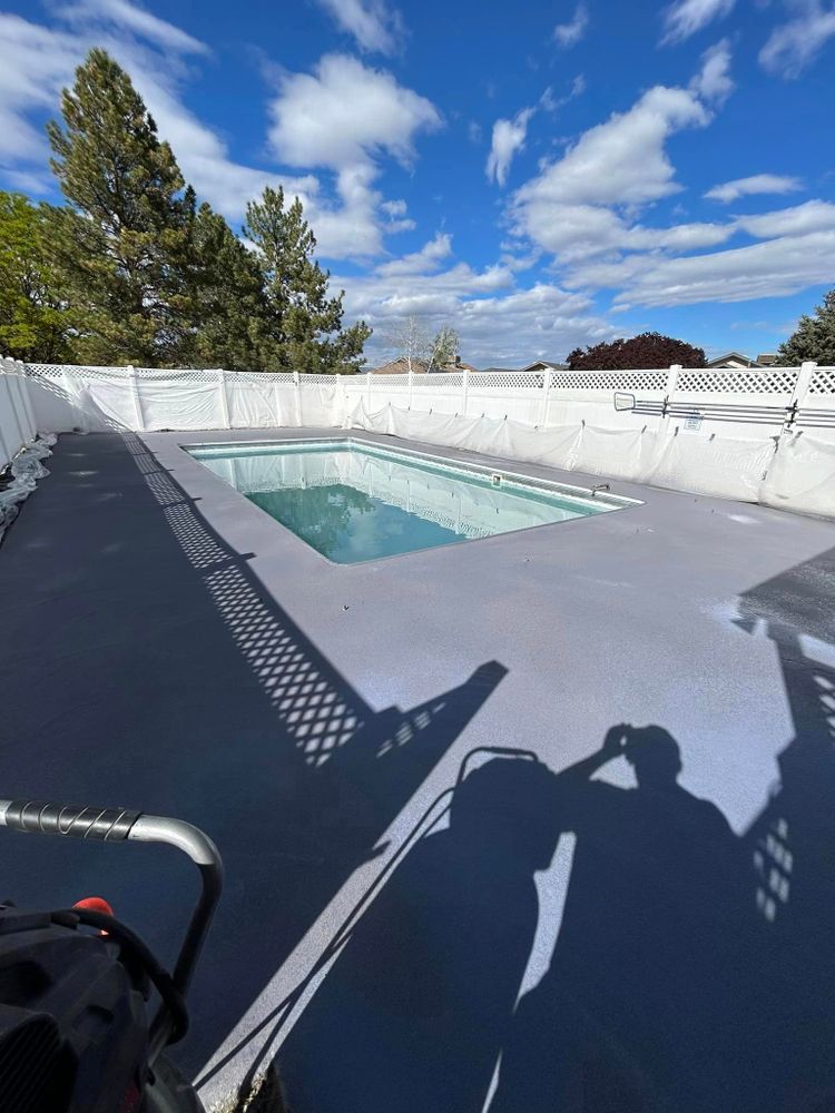 Gray-surfaced pool with water, surrounded by a white fence.