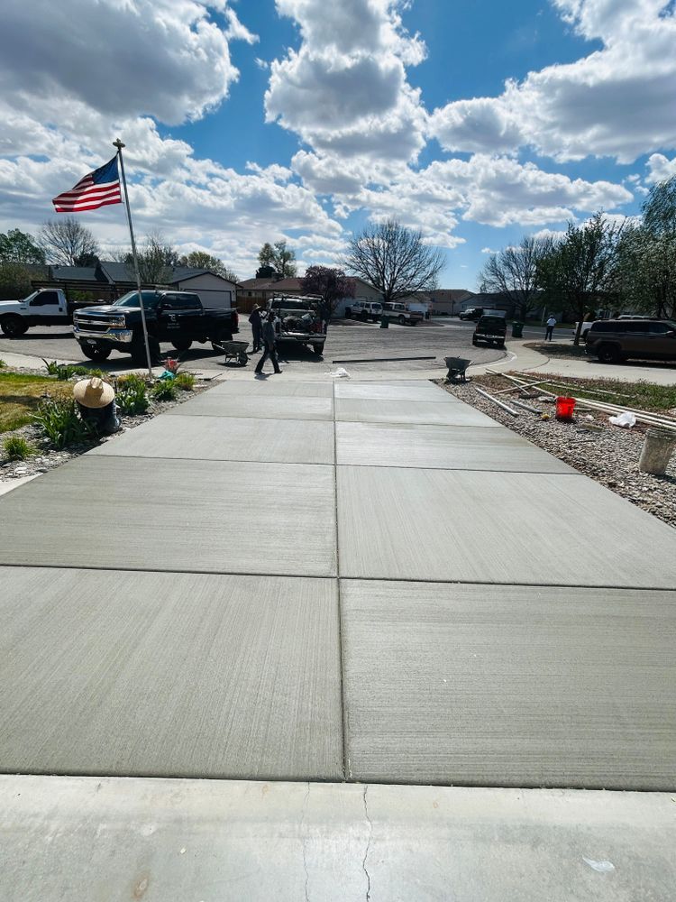 Freshly poured concrete driveway with workers, cars, flag, and cloudy sky.