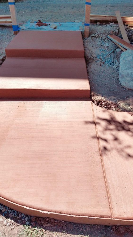 New reddish-brown concrete walkway and steps under construction outside.