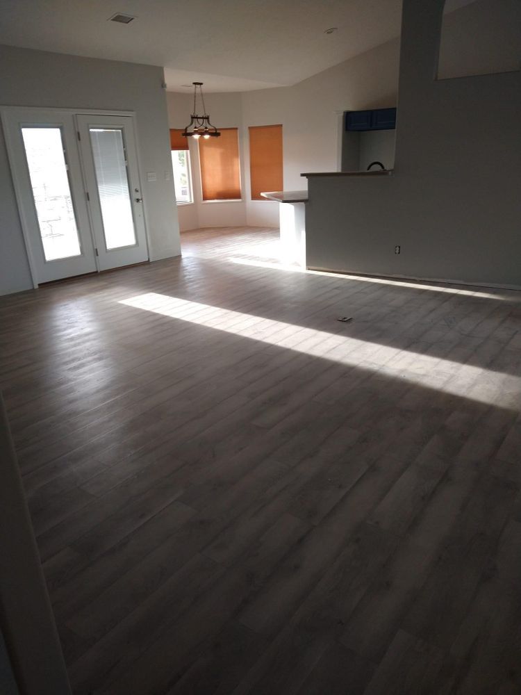 Empty sunlit room with light wood-look flooring, white walls, and French doors leading outside.