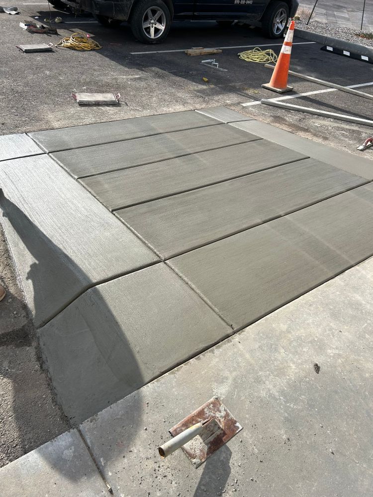 Freshly poured concrete sidewalk with rectangular slabs, near a parking lot.