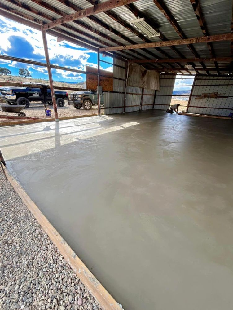 Newly poured concrete floor inside a metal-roofed structure with a truck and trailer visible outside.