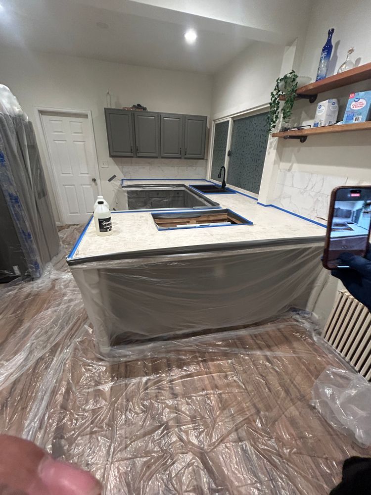 Kitchen with gray cabinets, a light countertop, and an island covered in plastic during renovation.
