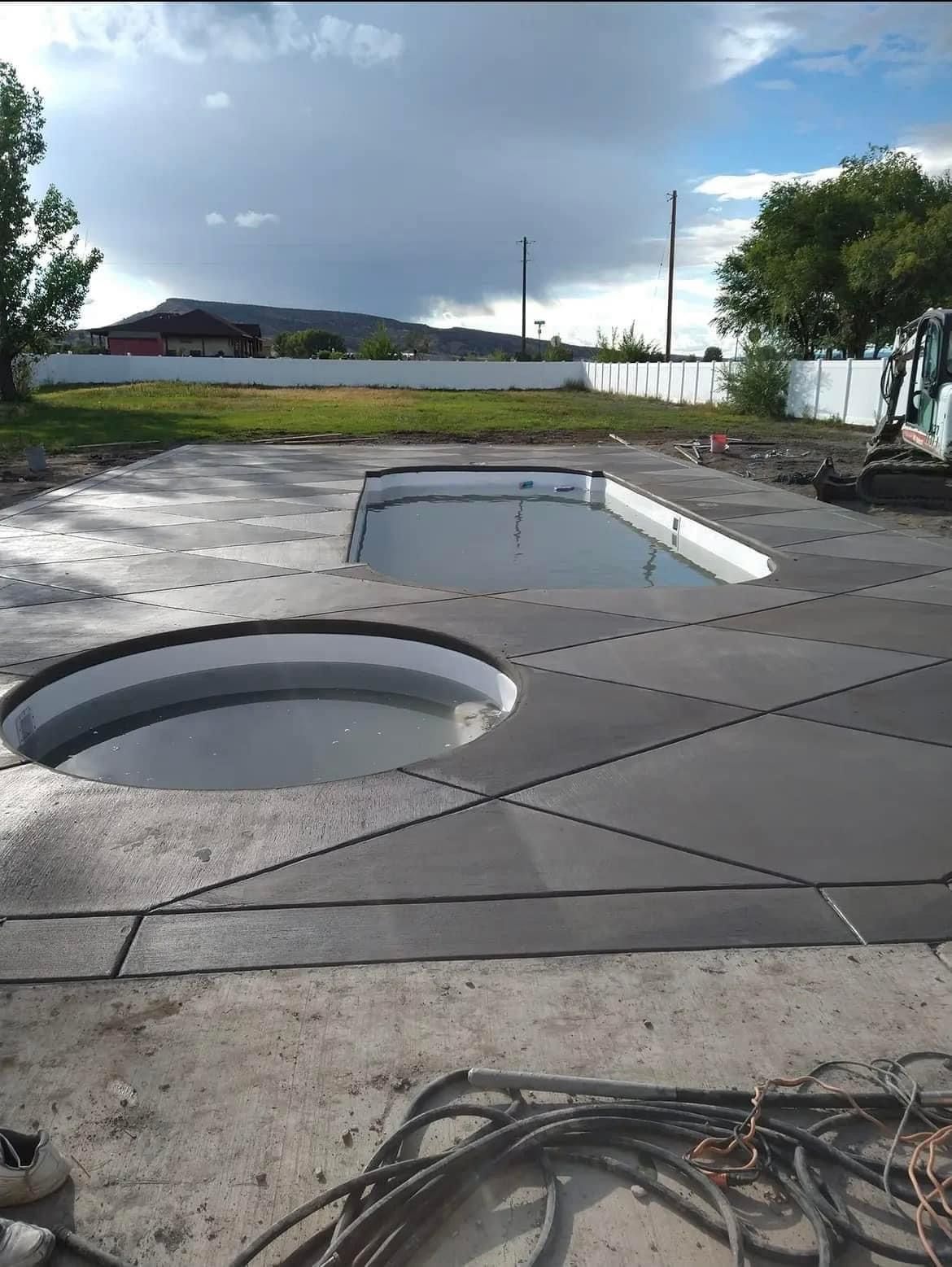Newly poured concrete around two pool openings, with a dark sky backdrop.