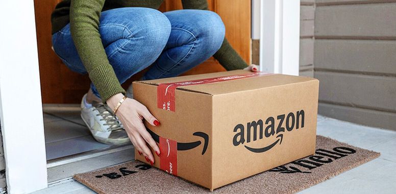 A woman is kneeling down to pick up an amazon box.