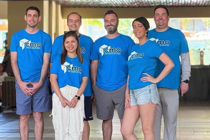 Group of seven people wearing matching blue shirts with a logo, standing outdoors.