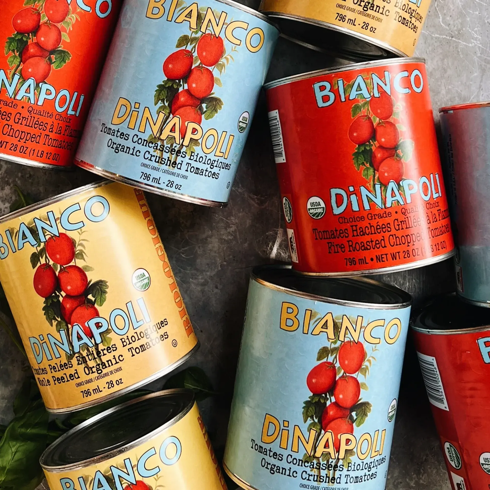 Cans of Bianco DiNapoli tomatoes in various colors.