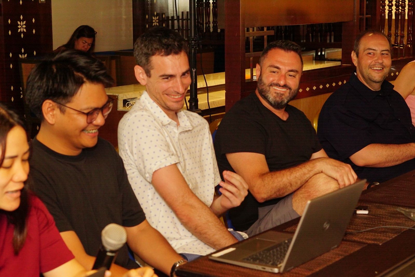Five people seated at a table, looking at a laptop and smiling. Interior shot.