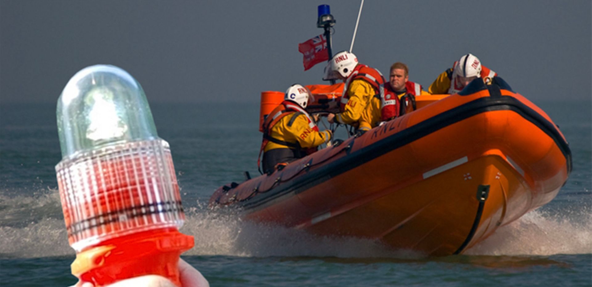 A rescue boat with orange hull and crew in yellow suits is underway, with a flashing light in the foreground.