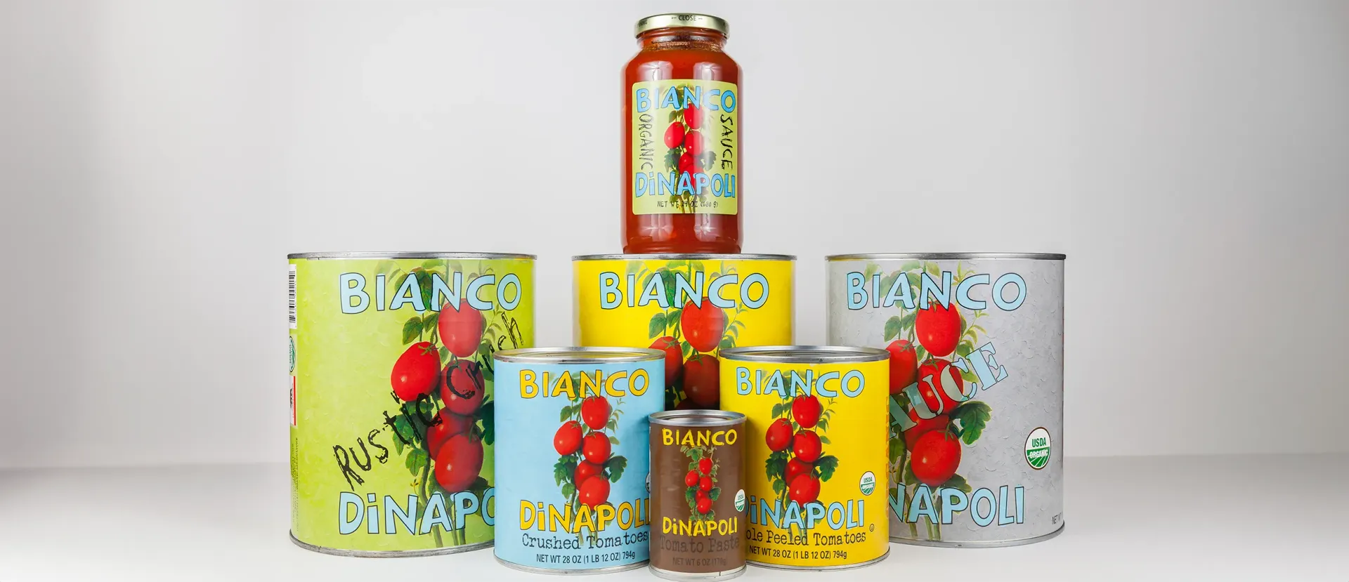 Canned tomatoes in various sizes and colors, arranged in a group with a jar of sauce on top.