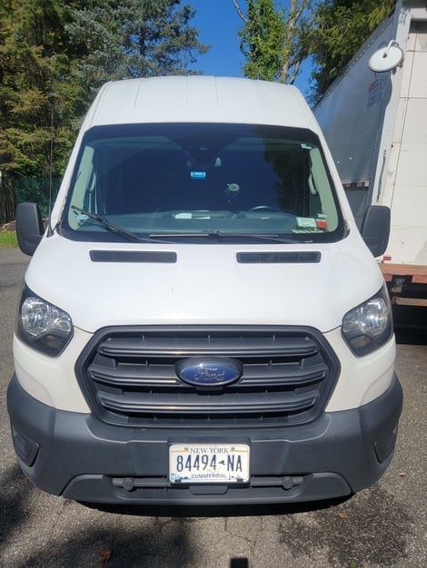 White Ford Transit van with a black grill and license plate, parked outdoors.