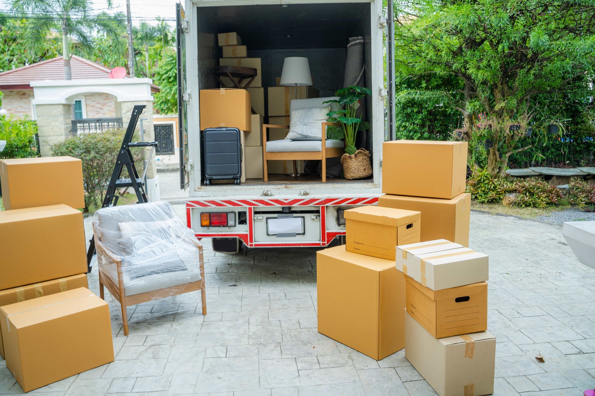 Moving truck being loaded with boxes and furniture in a driveway.
