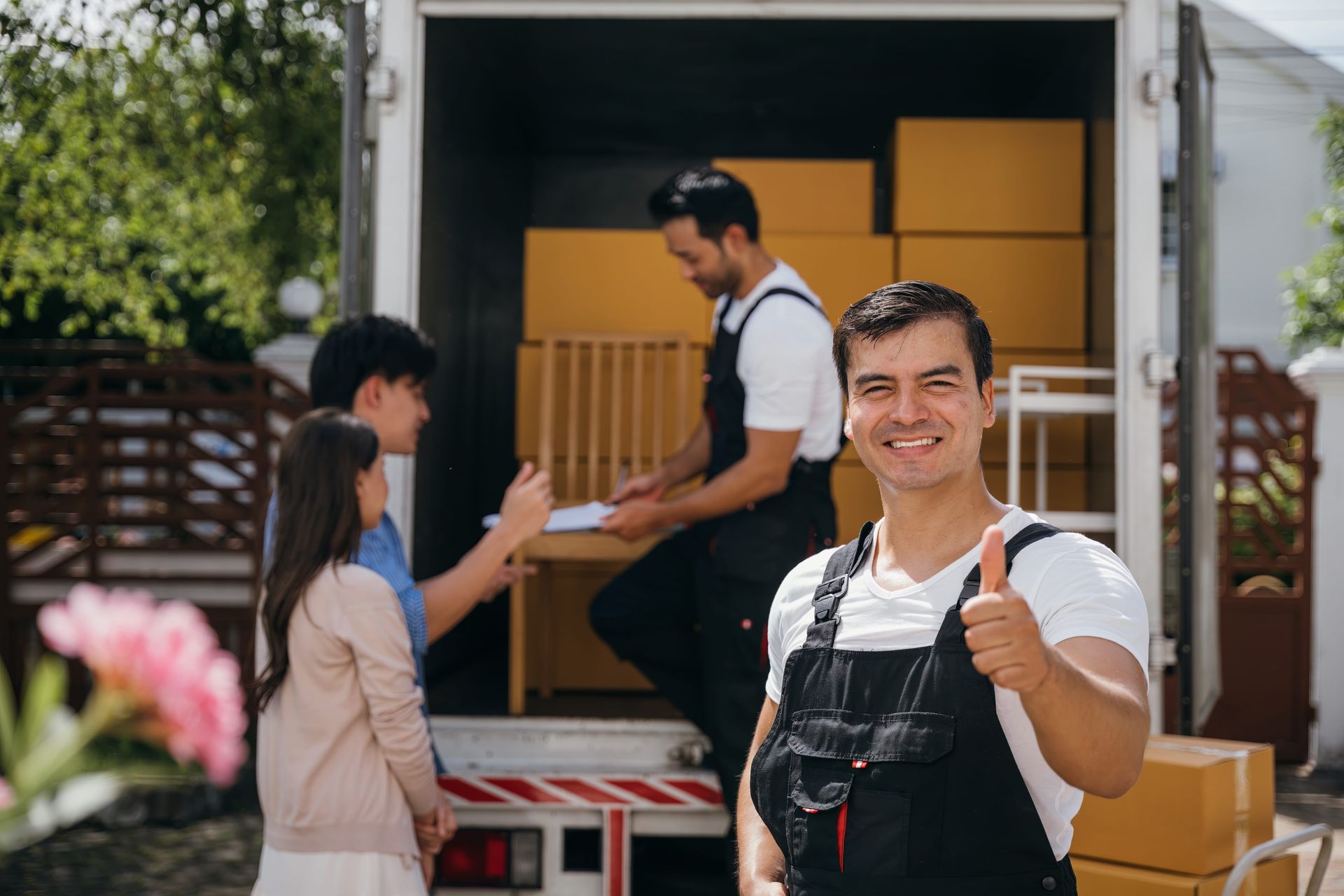 Movers loading boxes into a truck, with a smiling worker giving a thumbs up. A couple watches.