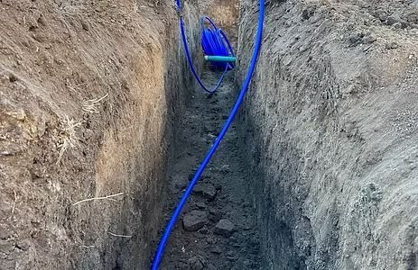 Blue utility lines in a narrow, freshly dug trench in the earth.