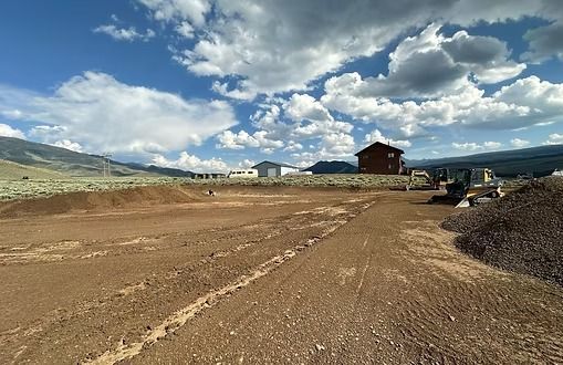 Dirt construction site with buildings in the background and cloudy sky.