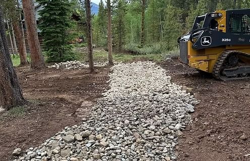 A gravel path under construction with a yellow skid steer in a wooded area.