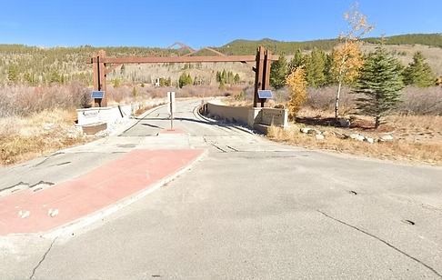 Entrance with a wooden archway, concrete posts, and a red-painted section; mountains in background.