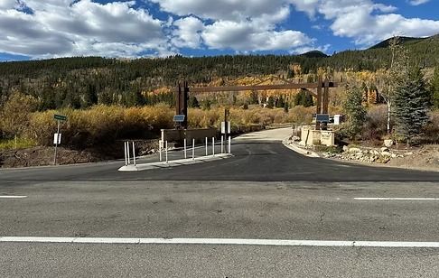 Asphalt road leading to an entrance with a wooden arch, mountain backdrop, fall foliage.