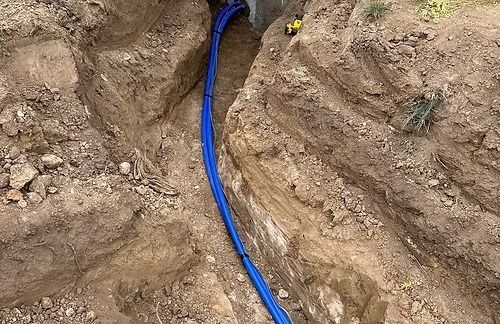 Trench with blue pipes installed; brown earth walls surround the trench.
