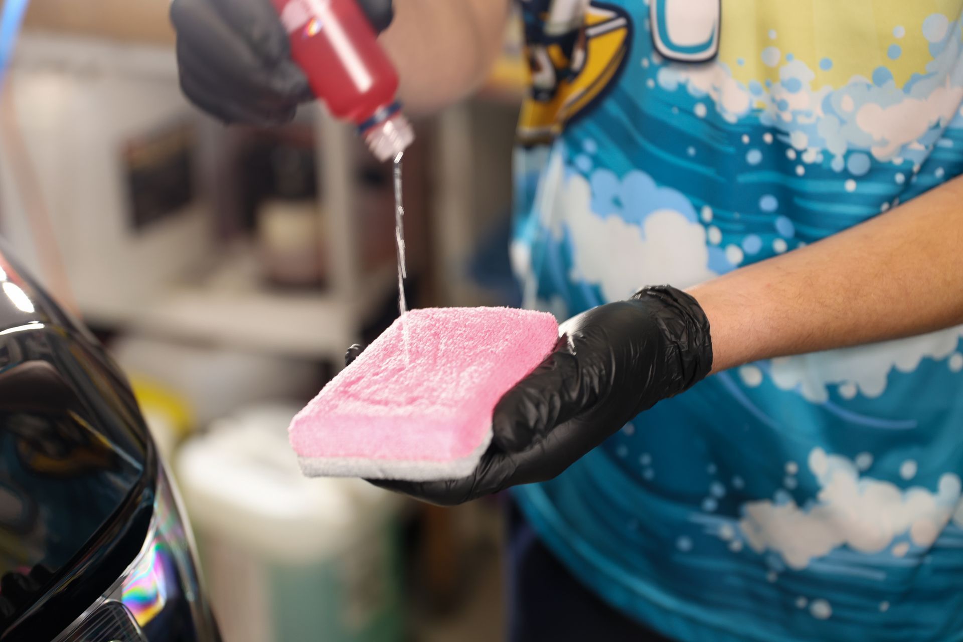 A person is holding a pink sponge in their hand and pouring liquid on it.