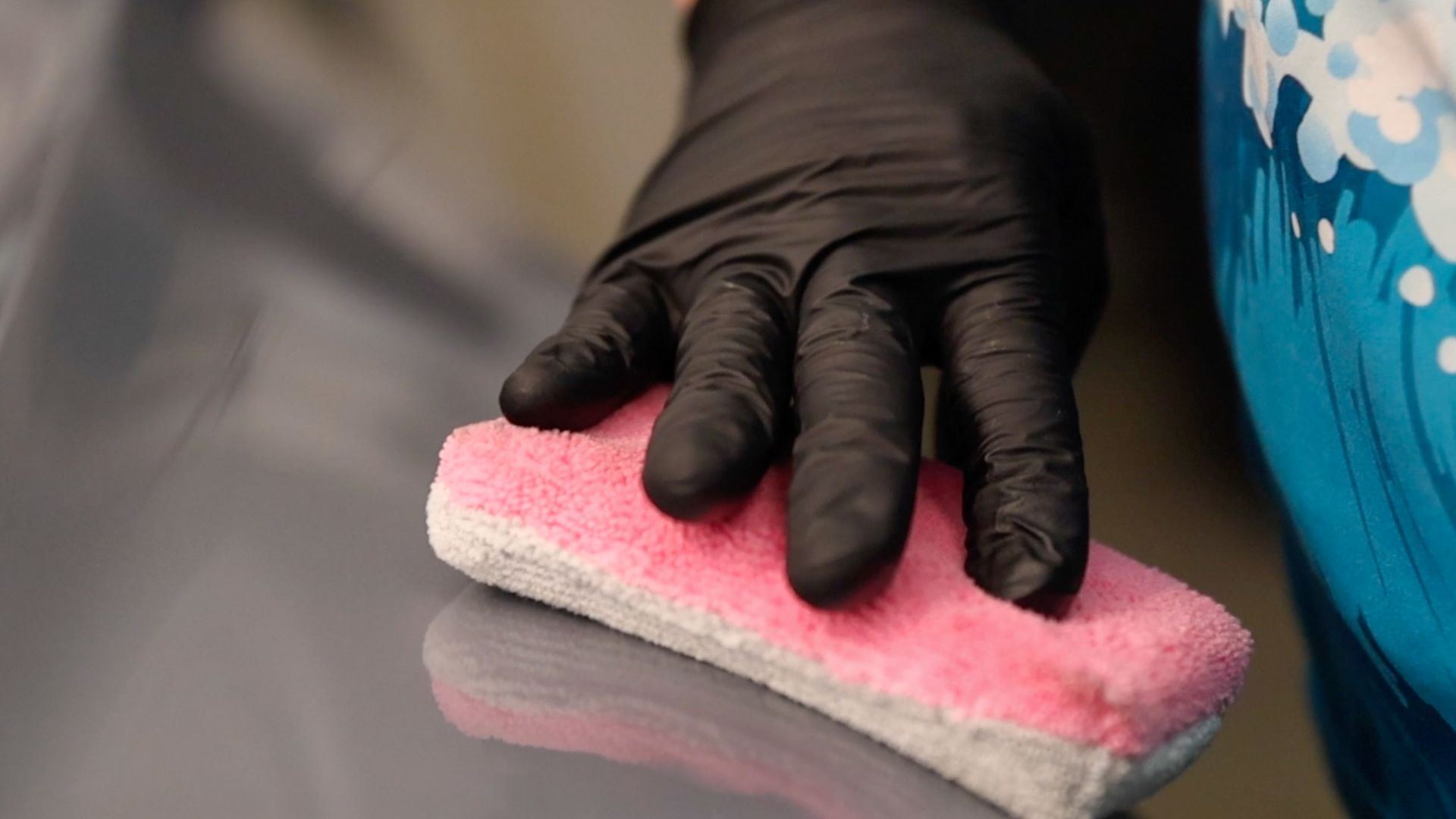 A person wearing black gloves is cleaning the steering wheel of a car.