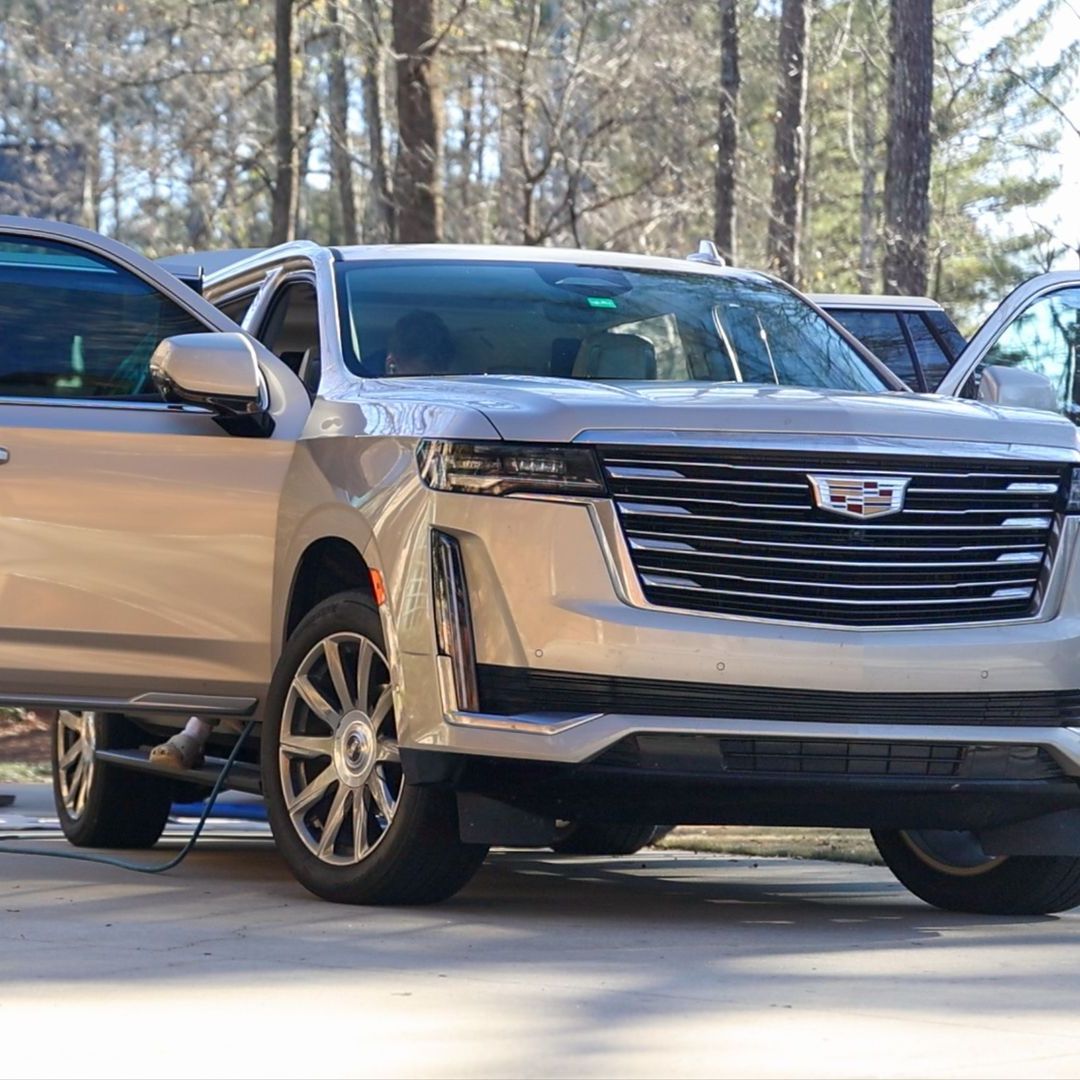 A silver car is parked in a parking lot next to a forest.