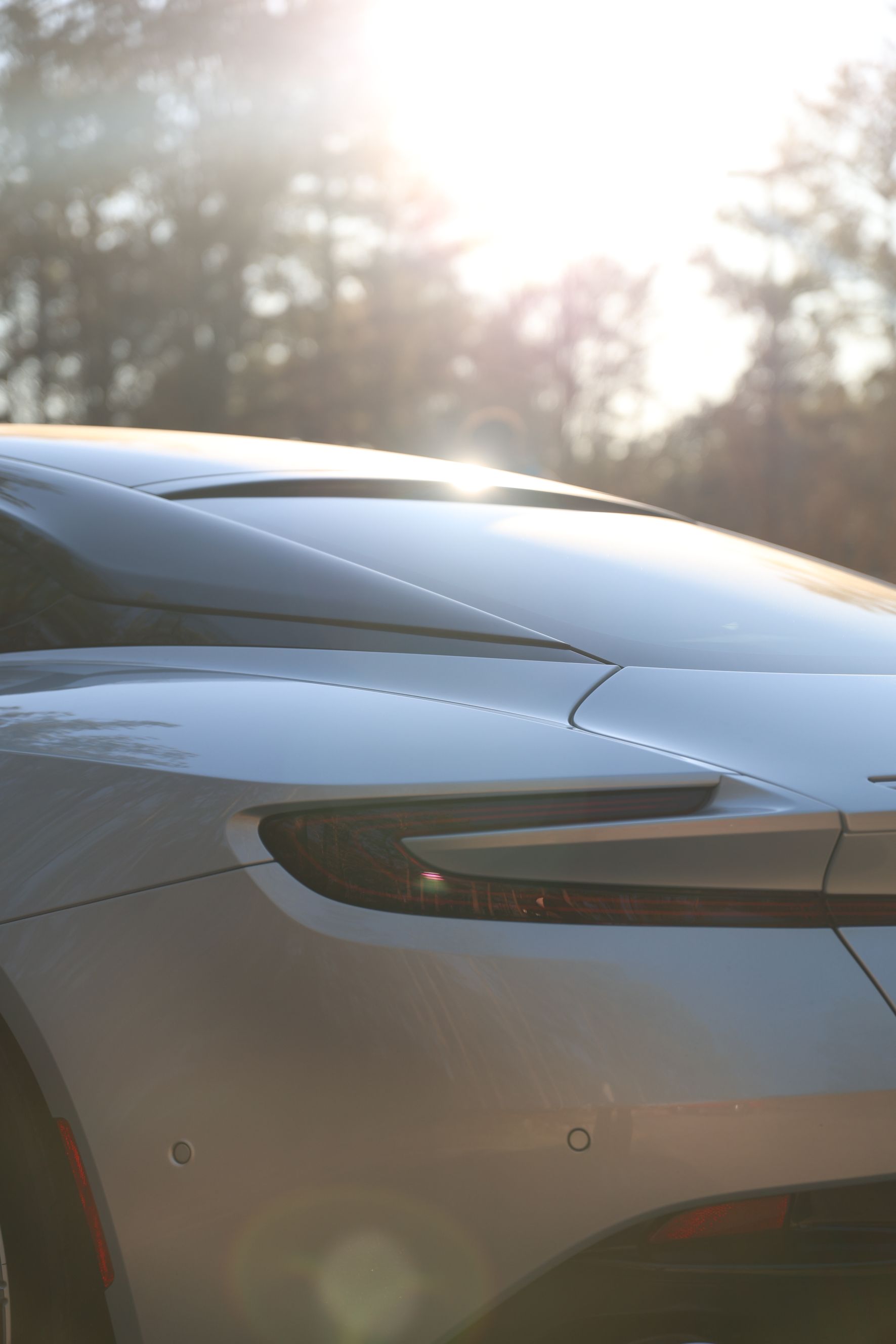 A close up of the rear end of a car with the sun shining through the trees in the background.