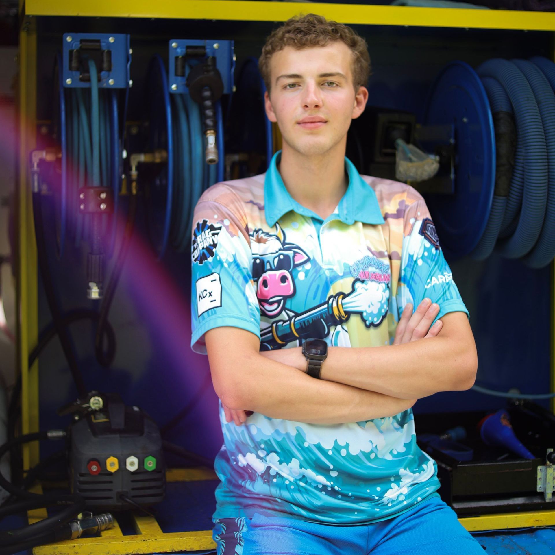 A young man is standing in front of a van with his arms crossed.