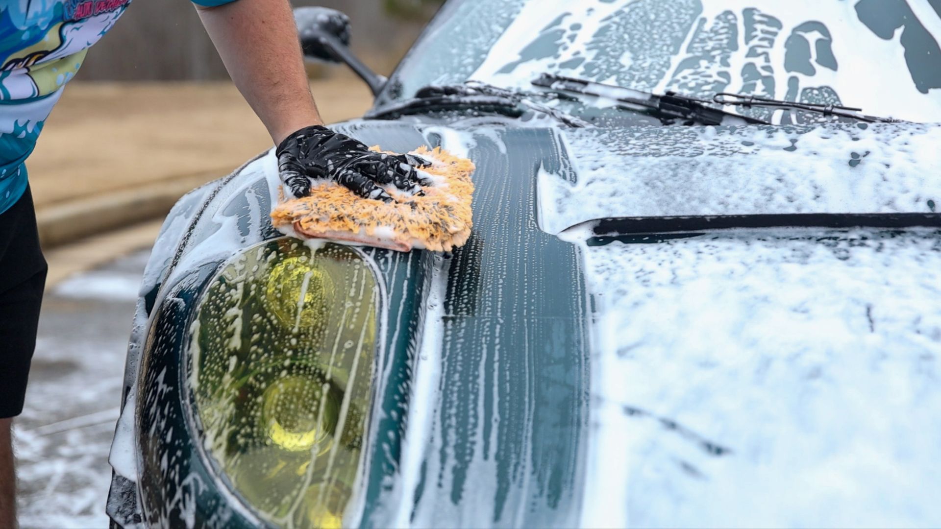A man is washing a car with a sponge in a garage.